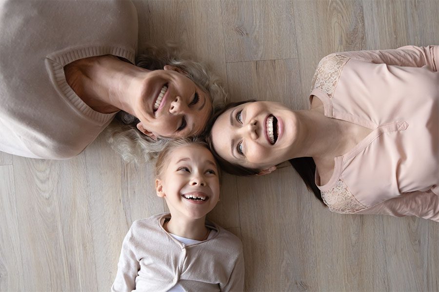 Client Center - Portrait of a Joyful Grandmother Mother and Daughter Laying on the Wooden Floor in Their Home