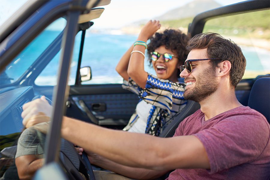 Insurance Quote - Portrait of Two Smiling Young Friends Having a Good Time Sitting in a Convertible by the Ocean on a Road Trip